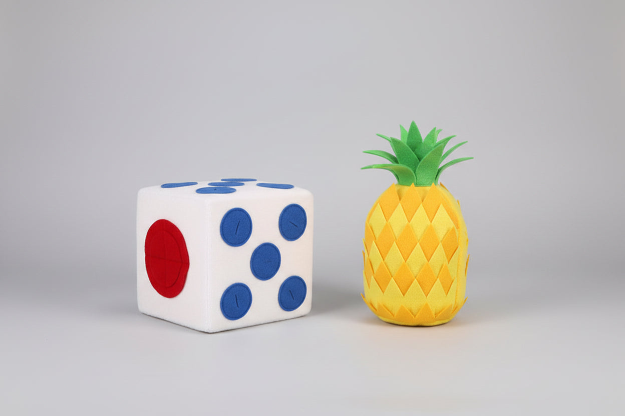 White die with blue, black, and red faces next to a yellow pineapple plush toy