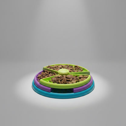A circular pet food bowl with three concentric rings in teal, purple, and lime green, filled with kibble, set against a dark background with a spotlight effect.